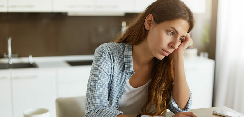 Young woman looking up, "can you refinance a personal loan?" on a laptop.