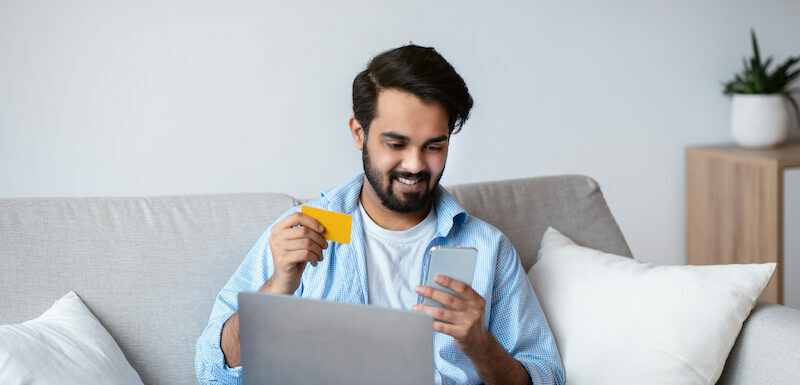 Young man choosing to purchase goods online with a credit card vs debit card.