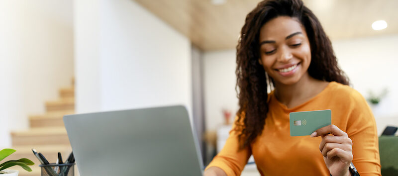Young woman holding up a plastic card trying to decide between a charge card vs credit card.