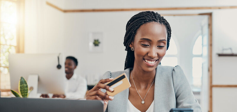 Young woman holding up credit credit looking up the answer to, "What is a good credit score?" on her phone.