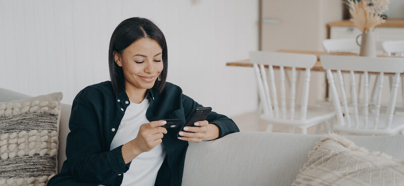 Woman smiling and holding a credit card after reading about improving her credit with a Nevly Money review.