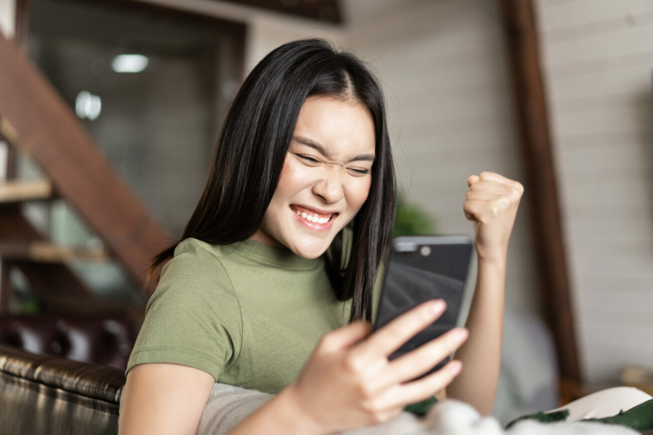 A woman smiling and celebrating while playing a game on her cell phone