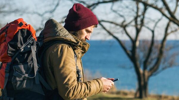 Hiking man near lake looking down at his phone.