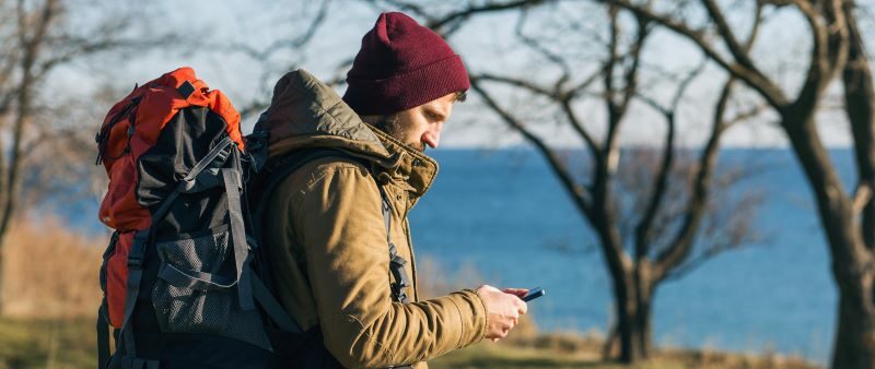 Hiking man near lake looking down at his phone.