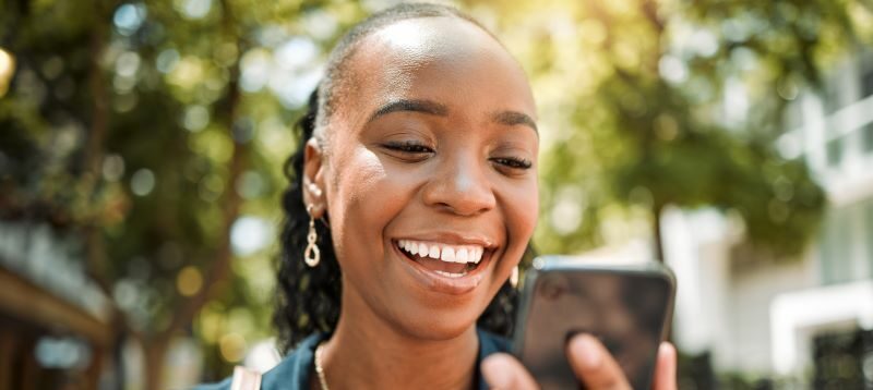 woman outside smiling at cell phone.