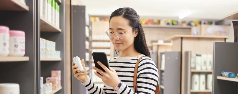 A woman holding an item off the store shelf while looking at her phone