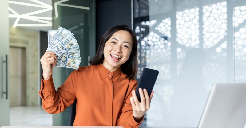 Woman smiling holding up cash and cell phone