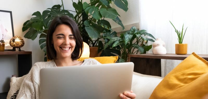 Woman on living room sofa smiling at laptop.
