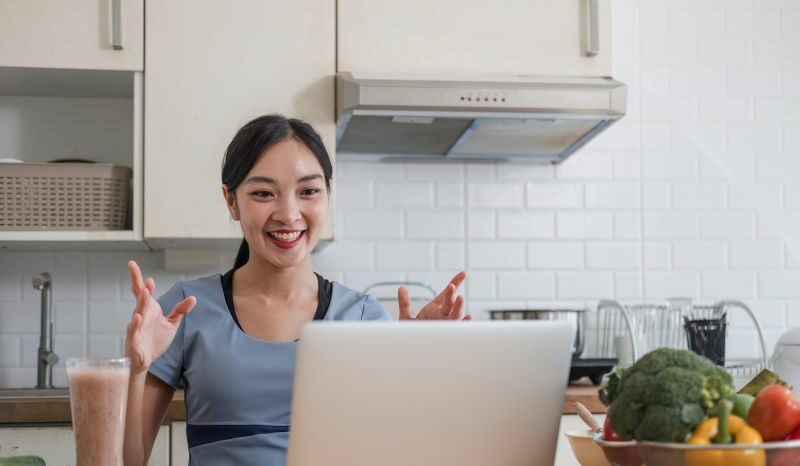 Woman in kitchen smiling at laptop