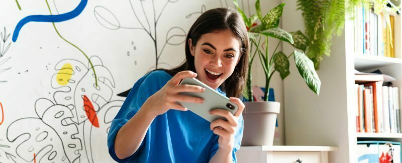 Young woman excited playing game on phone sitting on bed.