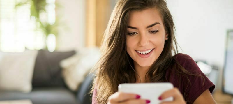 Woman sitting in living room smiling at cell phone