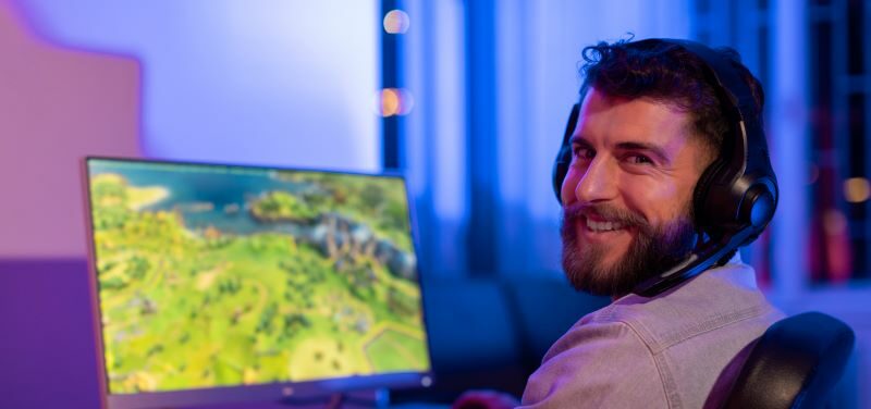 Man wearing headset playing computer game smiling back at camera