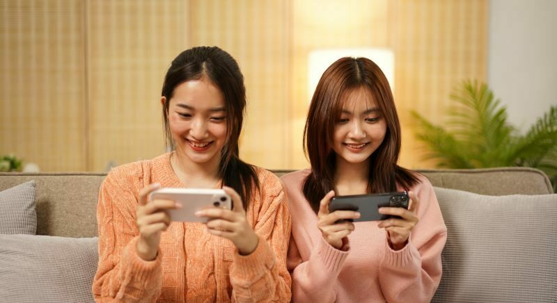 Two women sitting on sofa playing phone games