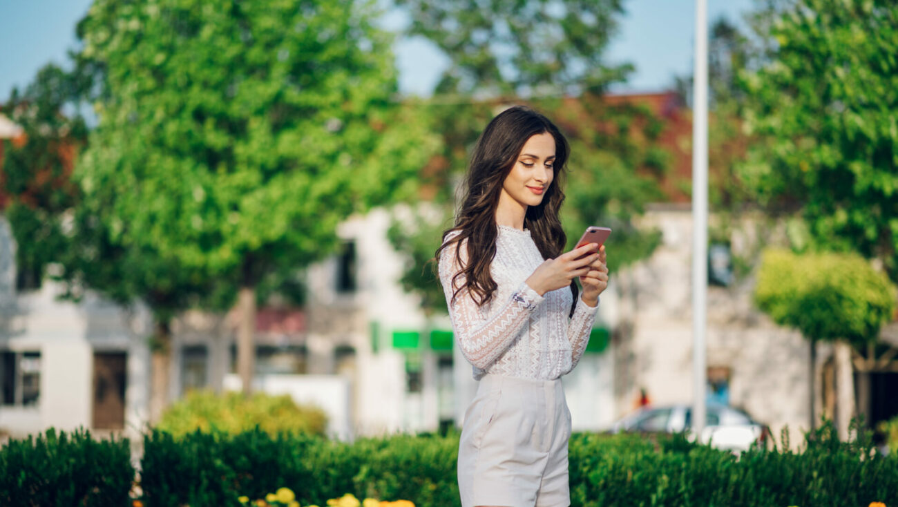Woman standing outside smiling at cell phone