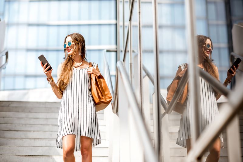 Woman walking in city smiling at cell phone
