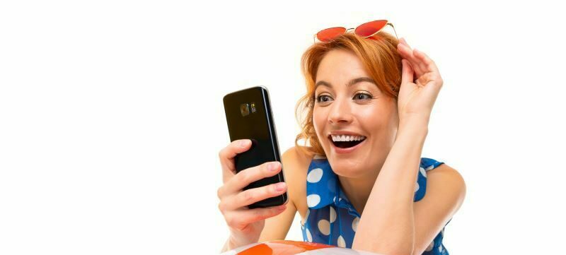 Woman with sunglasses on head leaning on beach ball and smiling at phone
