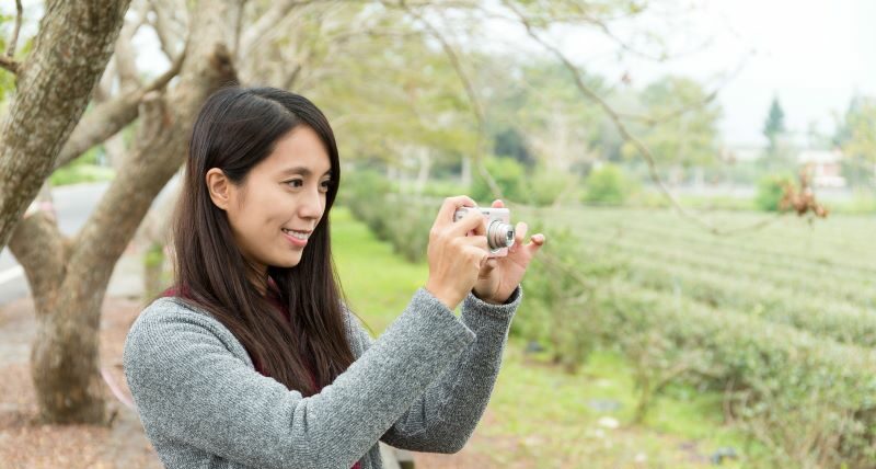 Woman outside smiling while taking a picture with a camera