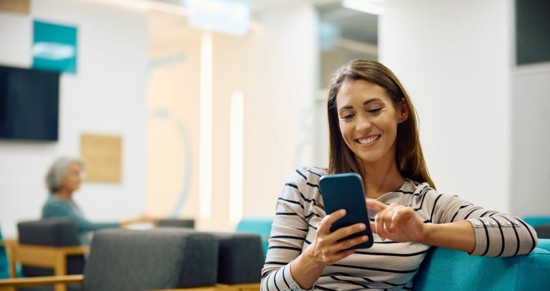 Woman sitting in waiting room smiling at cell phone