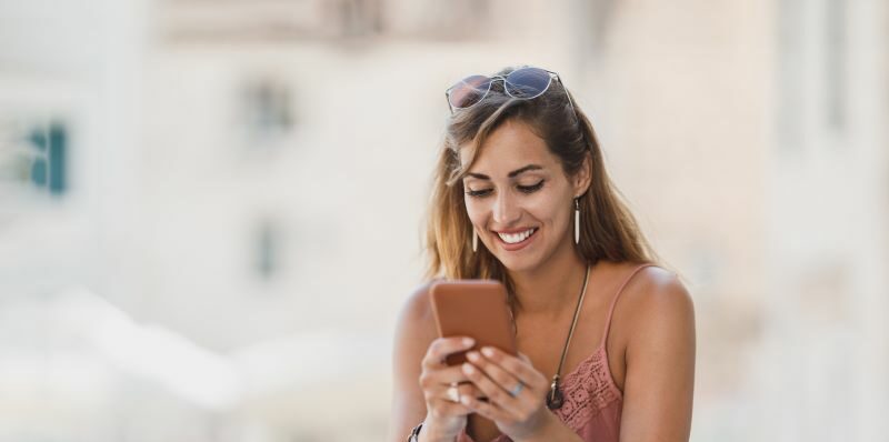 Woman sitting outside smiling at cell phone