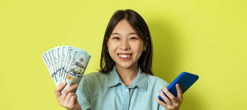 Woman smiling holding cash and a cell phone