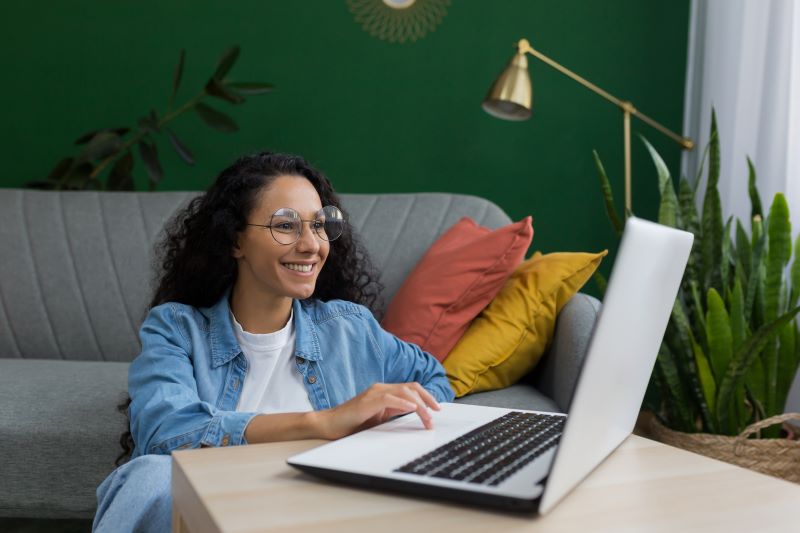 Woman sitting in living room smiling at laptop