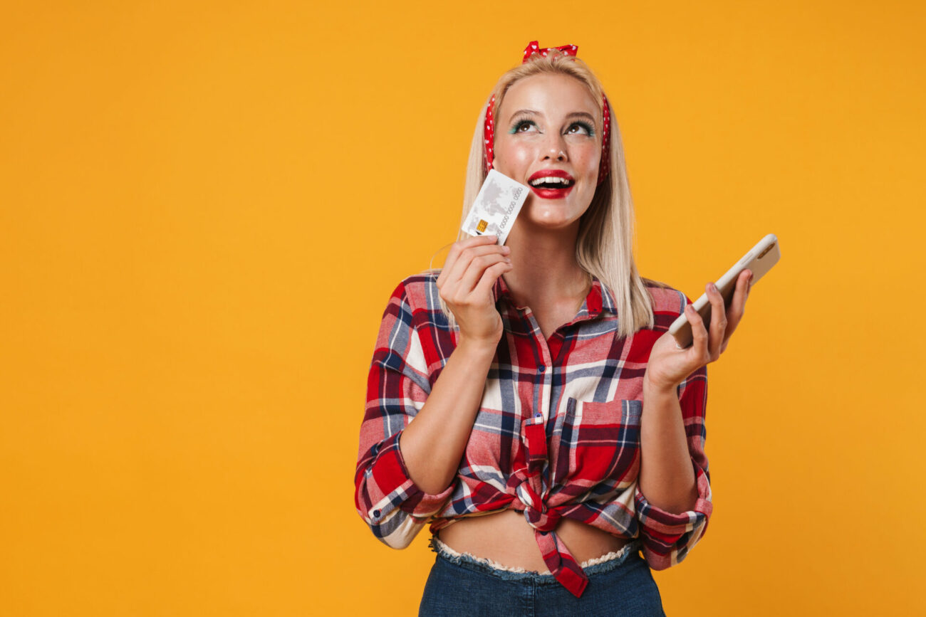 Happy young woman holds credit card and phone device