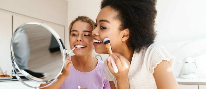 Young smiling women putting on makeup together