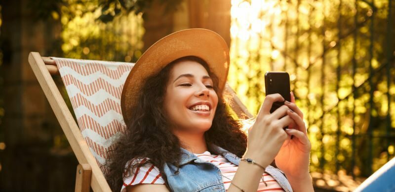 Woman lounging outdoors smiling at cell phone