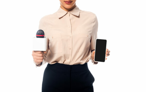 Woman against a white background holding a microphone in one hand and a cell phone in the other.