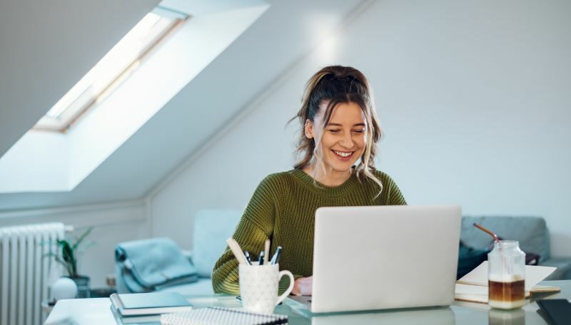 Woman at home office desk smiling at laptop
