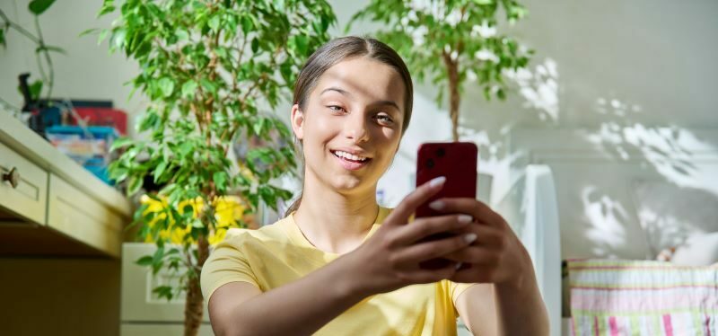 Woman smiling at cell phone with house plants in the background