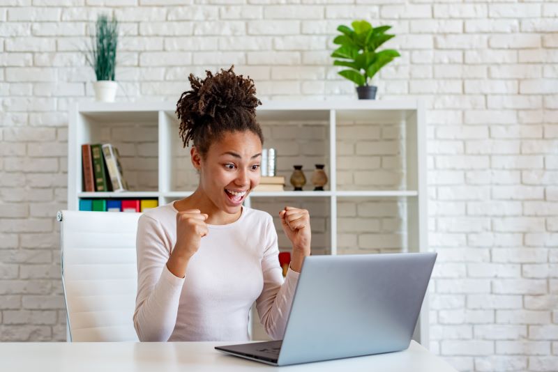 Woman sitting at home office desk laptop excited