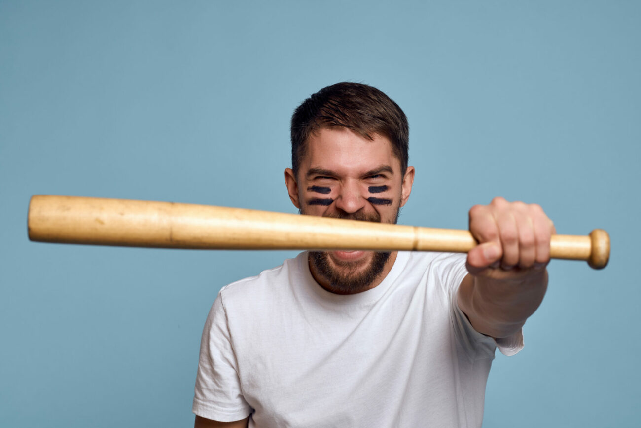 Man in mock "war paint" holds a baseball bat in his left outstretched hand and shouts.