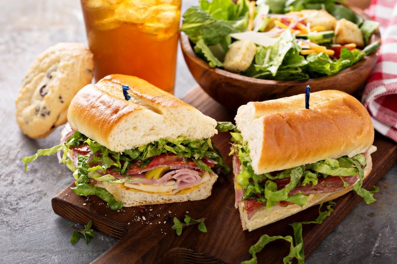 A sub sandwich sliced in half, a salad, and an iced tea