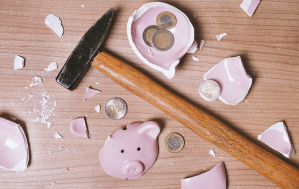 A hammer lies among the pieces of a shattered piggy bank and a few coins.