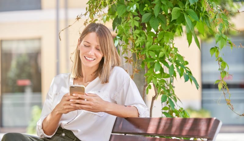 Woman sitting on bench outdoors smiling at cell phone