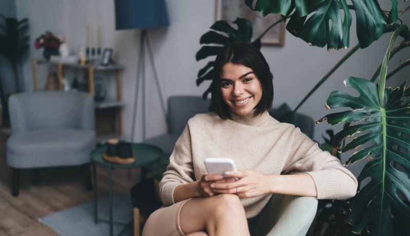 Woman lounging with cell phone in livingroom chair smiling at the camera