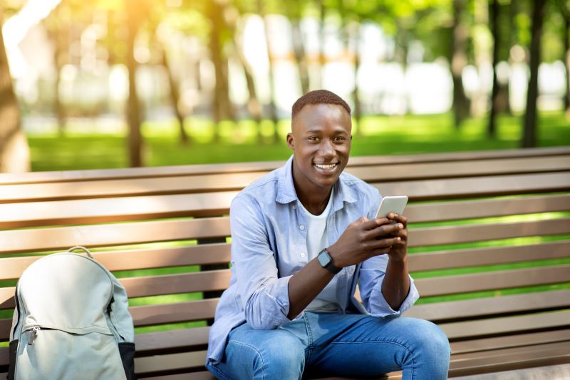 Man sitting on park bench holding cell phone smiling at the camera
