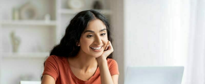 Woman sitting at laptop at home smiling