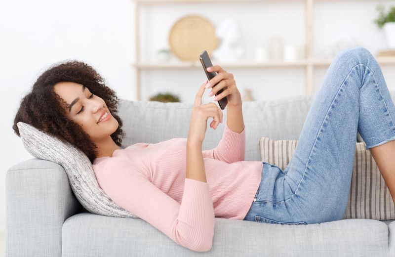 Woman lying on sofa smiling at cell phone