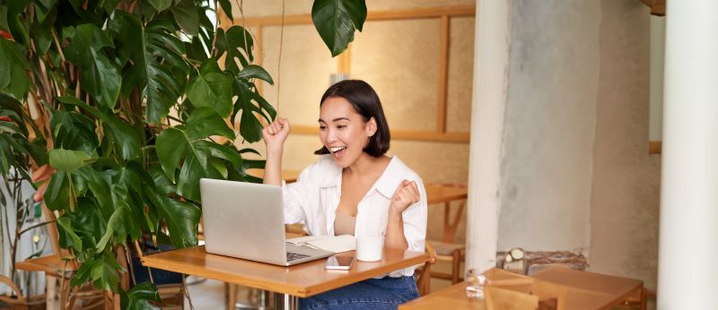 Woman smiling and raising fists to celebrate at laptop