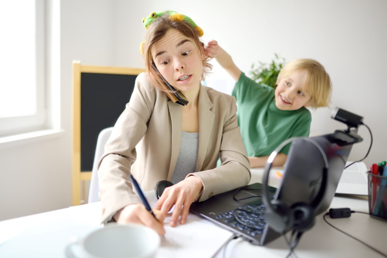 Working mom at desk struggles to take notes as her fun-loving child tugs at her left ear.