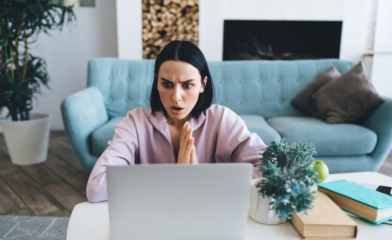 woman in living room looking at laptop shocked