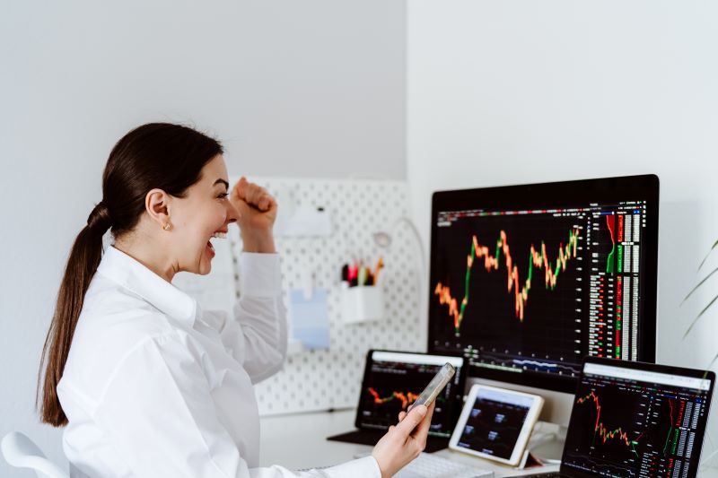 Excited woman looking at screens displaying stock charts