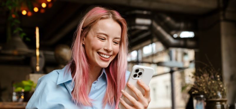 Woman holding coffee and smiling at phone in cafe