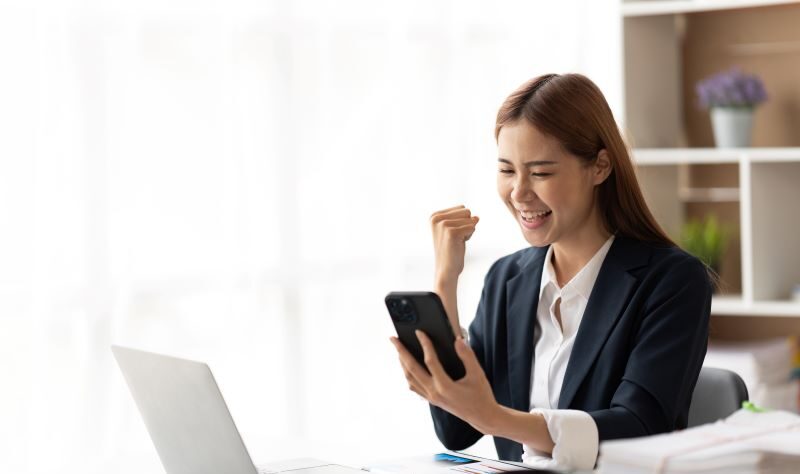 Woman sitting at desk looking at phone celebrating